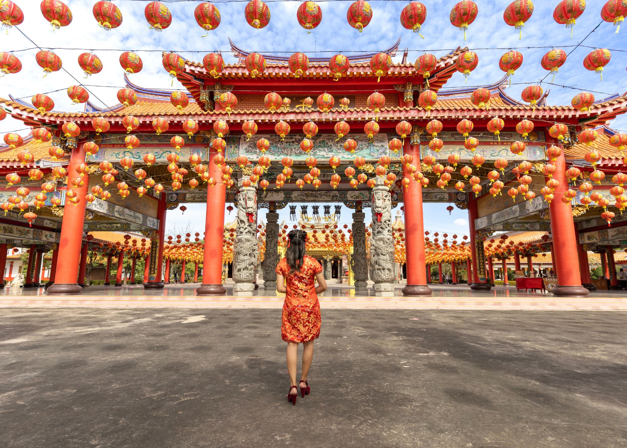 A woman dressed in a red and gold dress looking at Lunar New Year decor surrounding a temple.