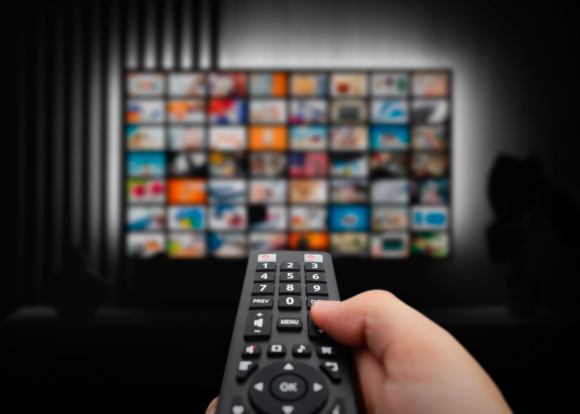 A person holding a tv remote toward a tv with streaming services listed.